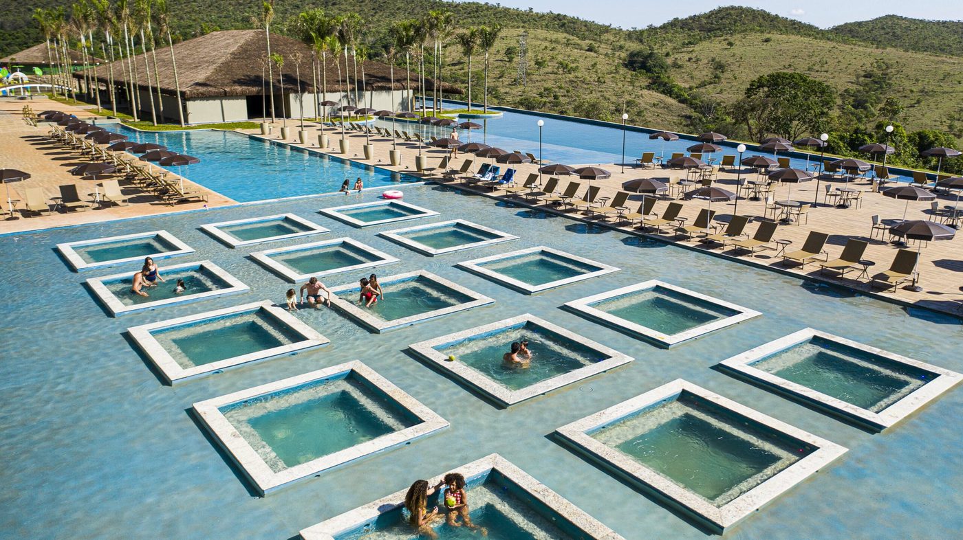 Vista aérea das piscinas de um resort da Rede Tauá, com hóspedes nas prainhas e a serra ao fundo